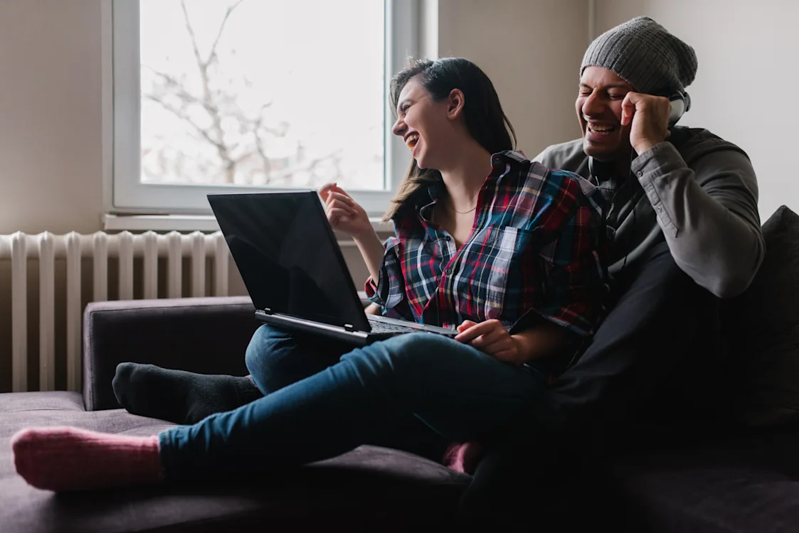 5G + fiber = sant Bildet viser en kvinne og en mann som sitter i en sofa og ler med en laptop på fanget
