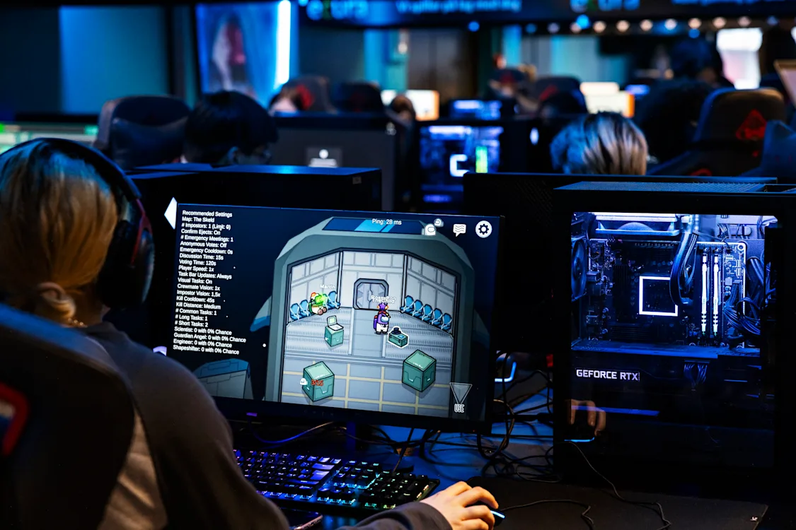 spillere Ryggen på en ungdom som sitter på en skjerm og gamer. Foran henne sitter mange andre ungdommer og gjør det samme.