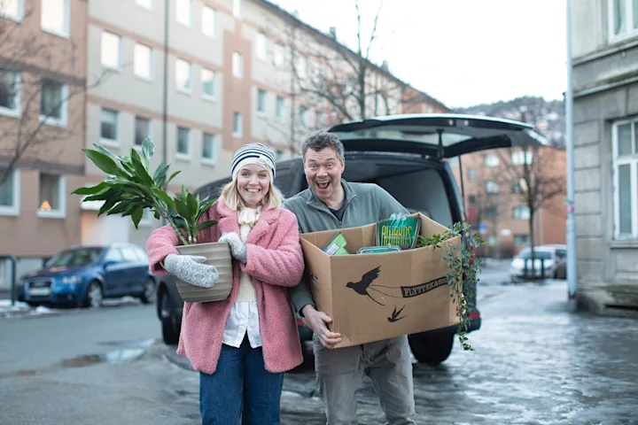 Et par står med flytteesker foran en boligblokk Et par står med flytteesker foran en boligblokk