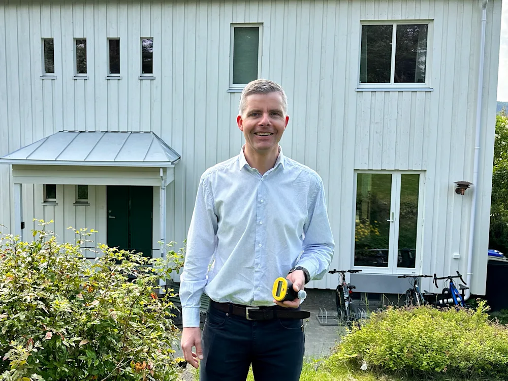 Smilende mann som holder en vannmåler i hendene står foran et bolighus Smilende mann som holder en vannmåler i hendene står foran et bolighus