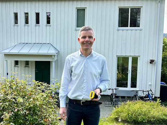 Smilende mann som holder en vannmåler i hendene står foran et bolighus Smilende mann som holder en vannmåler i hendene står foran et bolighus