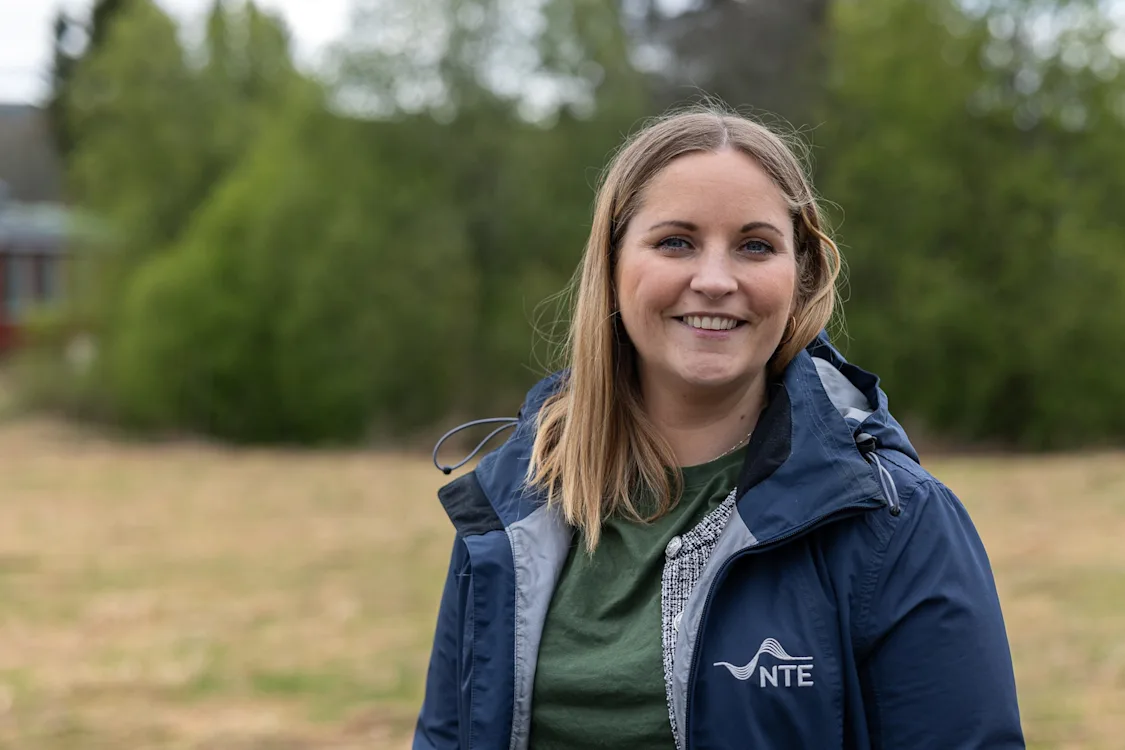 ranja vassli Smilende dame med halvlangt hår og jakke med NTE-logoen på står foran en treklynge