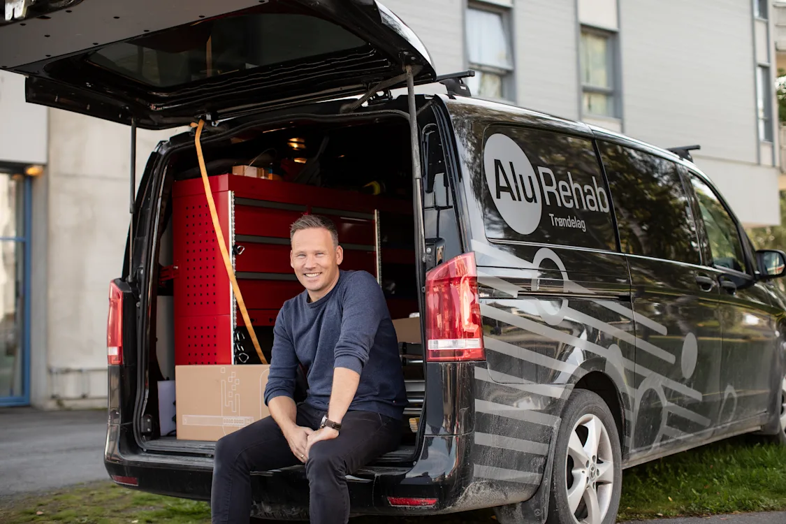 Tore Forbord sitter i bilen En smilende mann sitter i bagasjerommet på en varebil