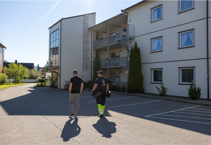Bilde som viser ryggen til en mann og en elektriker som går fra en parkeringsplass mot en boligblokk i et borettslag.
