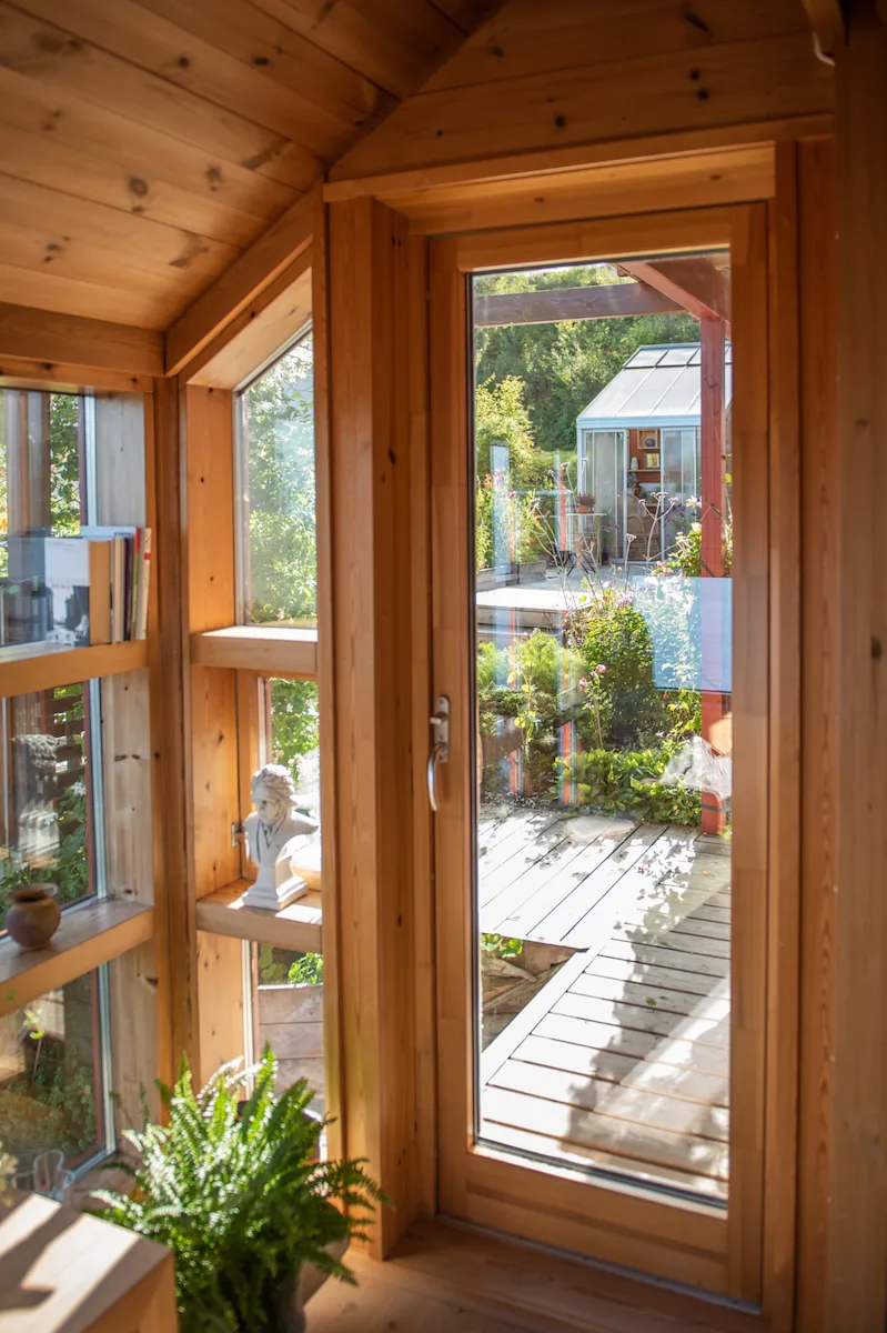 utsikt til hagen Utsikten gjennom glasset i en verandadør mot en hage med platting og drivhus
