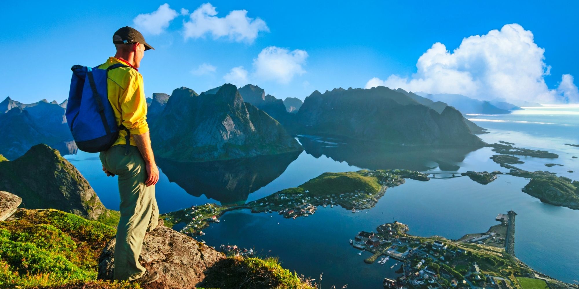 Mann ser ned på bebyggelse ved norsk fjord fra toppen av et fjell.