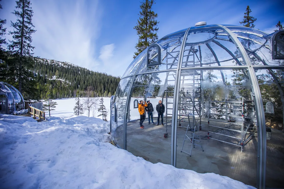 Gapahuk på Rypetoppen Tre menn står inne i en toetasjes gapahuk plassert midt i naturen med fjell, skog og snø på alle kanter