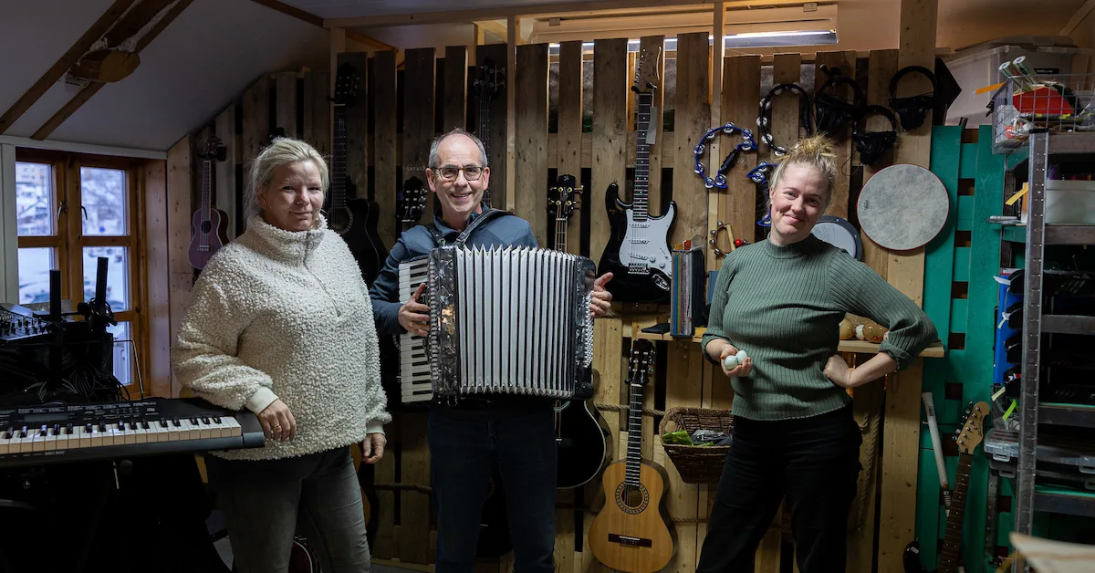 musikkbua To damer og en mann som holder et trekkspill står foran en vegg med instrumenter