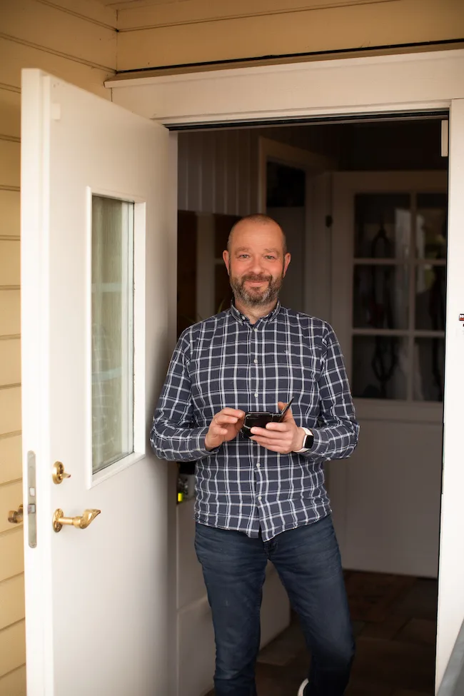 per-arvid wold med mobil Mann i rutete skjorte står i døråpningen og holder en mobiltelefon