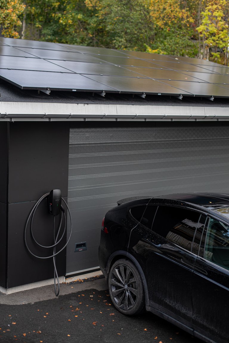 Bilde av en Tesla som blir ladet av solceller på garasjetak