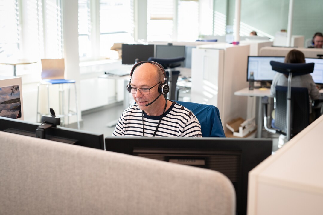 Bilde av en mann med headset som sitter bak to dataskjermer.