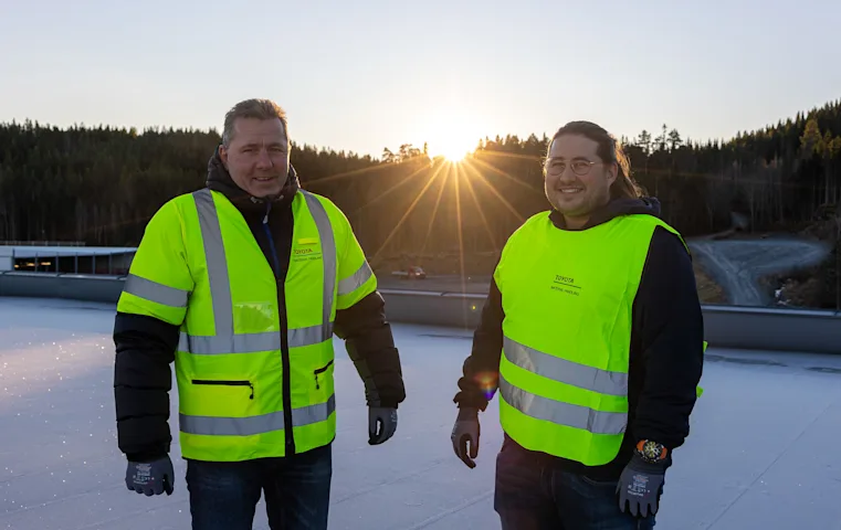 To blide menn med refleksvest med sola mellom seg To blide menn med refleksvest med sola mellom seg