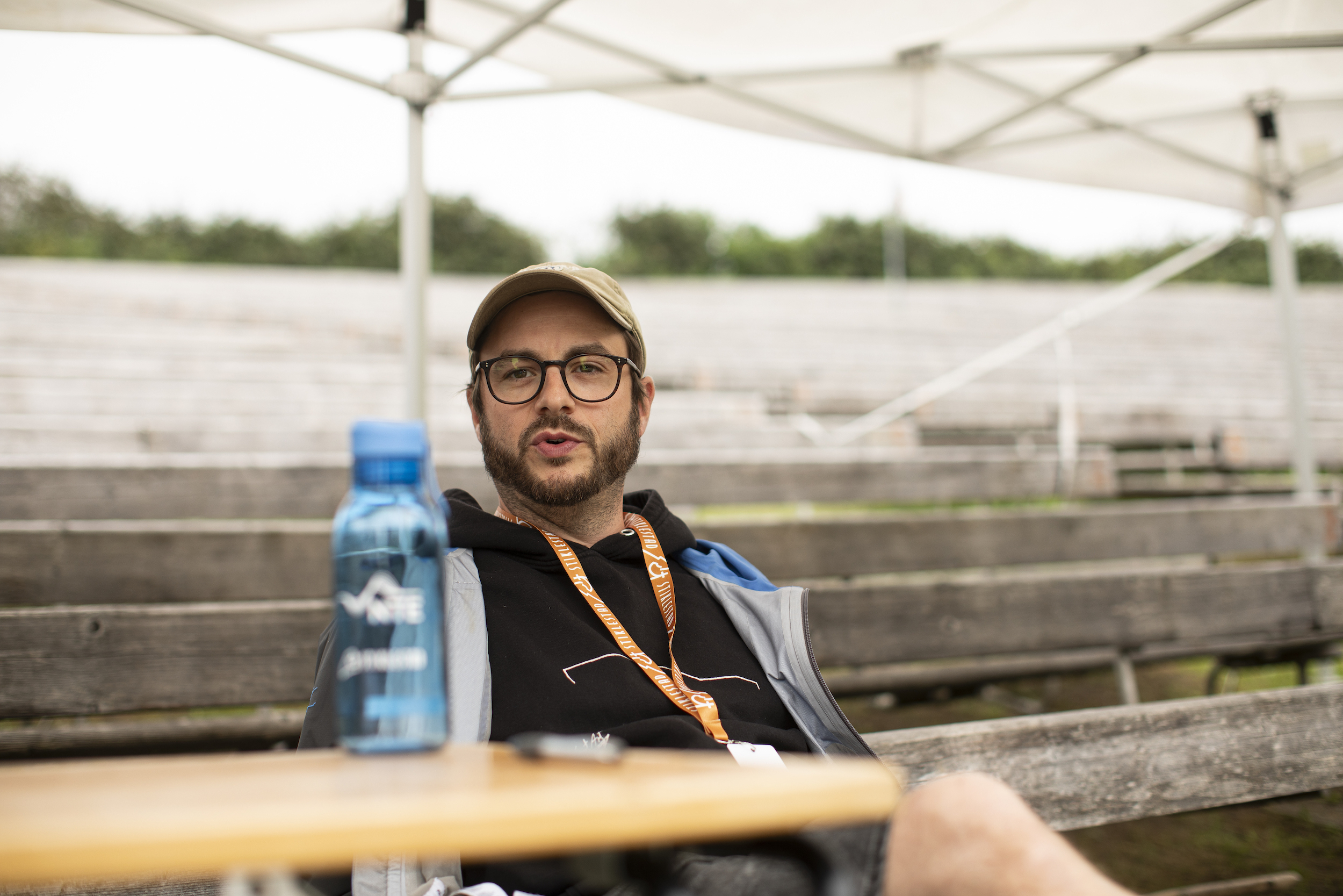 Mann med caps sitter på en benk med en vannflaske på et bord foran seg