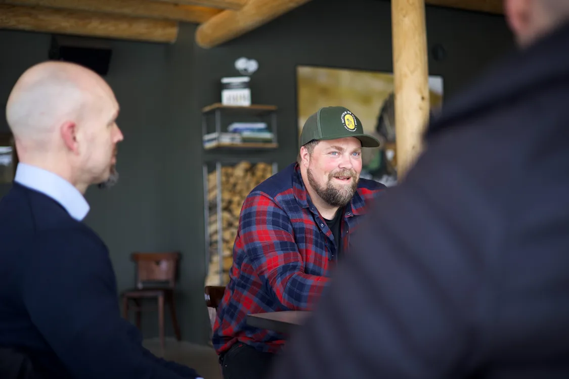 Ole Fredrik Haarsaker Smilende mann med caps i samtale med to menn du ser bakhodet på