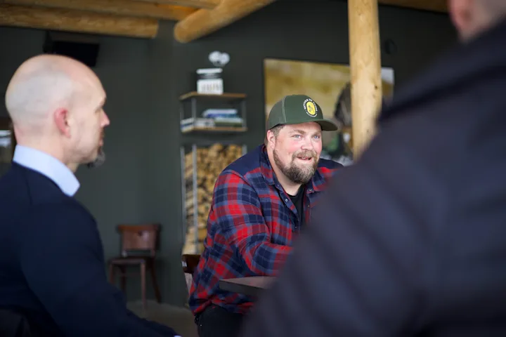 Smilende mann med caps i samtale med to menn du ser bakhodet på Smilende mann med caps i samtale med to menn du ser bakhodet på