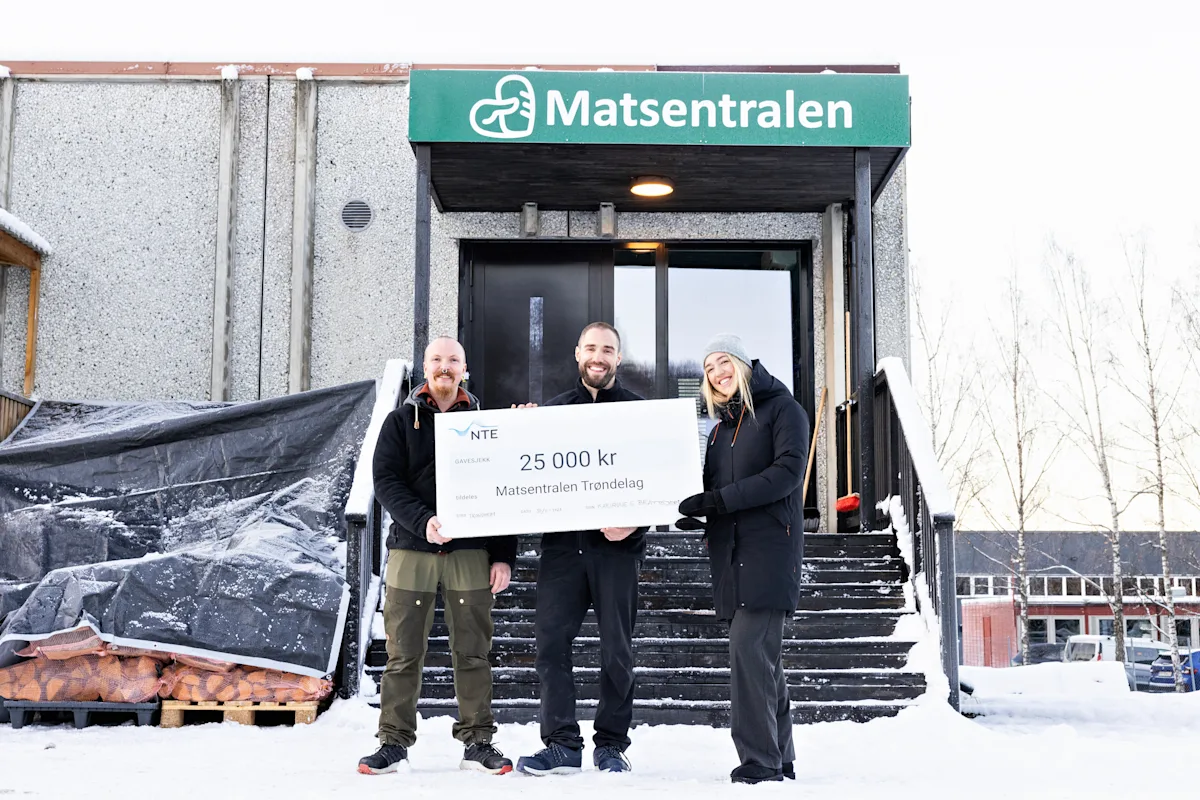 bilde med sjekken Tre mennesker holder en sjekk på 25 000 kroner mellom seg. De står under et skilt det står Matsentralen på.