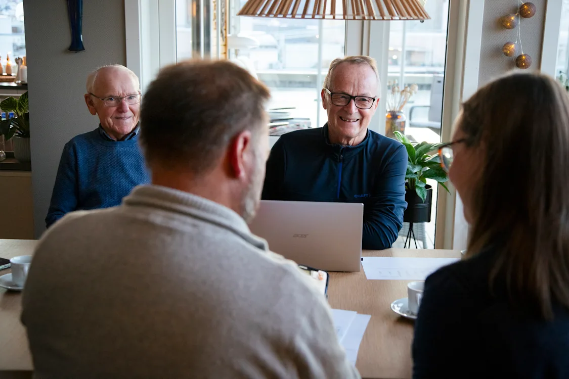 Tore og Dieter To smilende menn i samtale med en mann og en dame som sitter med ryggen til.