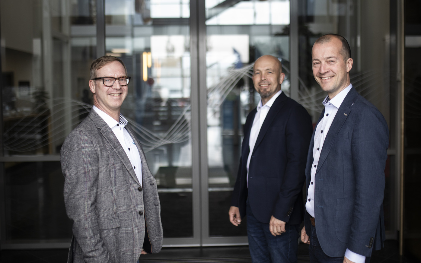 Bilde av tre menn i dress ved inngangsparti til bygning
