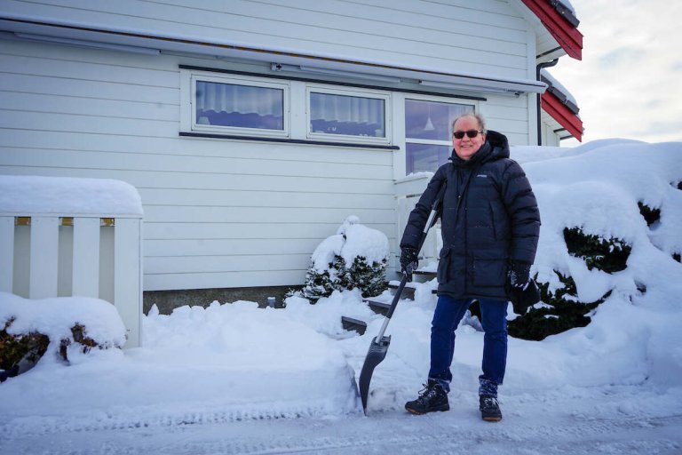 Mann som måker snø utenfor et hus