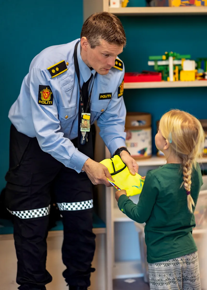 ole deler ut refleksvest Politimann deler ut refleksvest til en jente med lang flette
