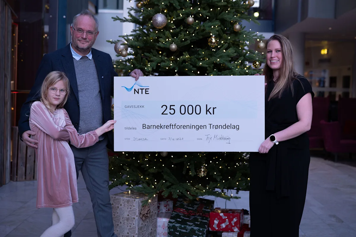 formell overrekkelse av sjekken Mann, kvinne og jente står foran et juletre og holder en sjekk på 25 000 kroner