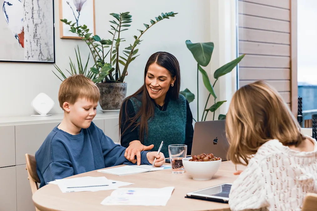 Mor og barn gjør lekser Bilde av mor og to barn som sitter ved et bord. Mor hjelper sønnen med lekser. Datteren ser på et nettbrett.