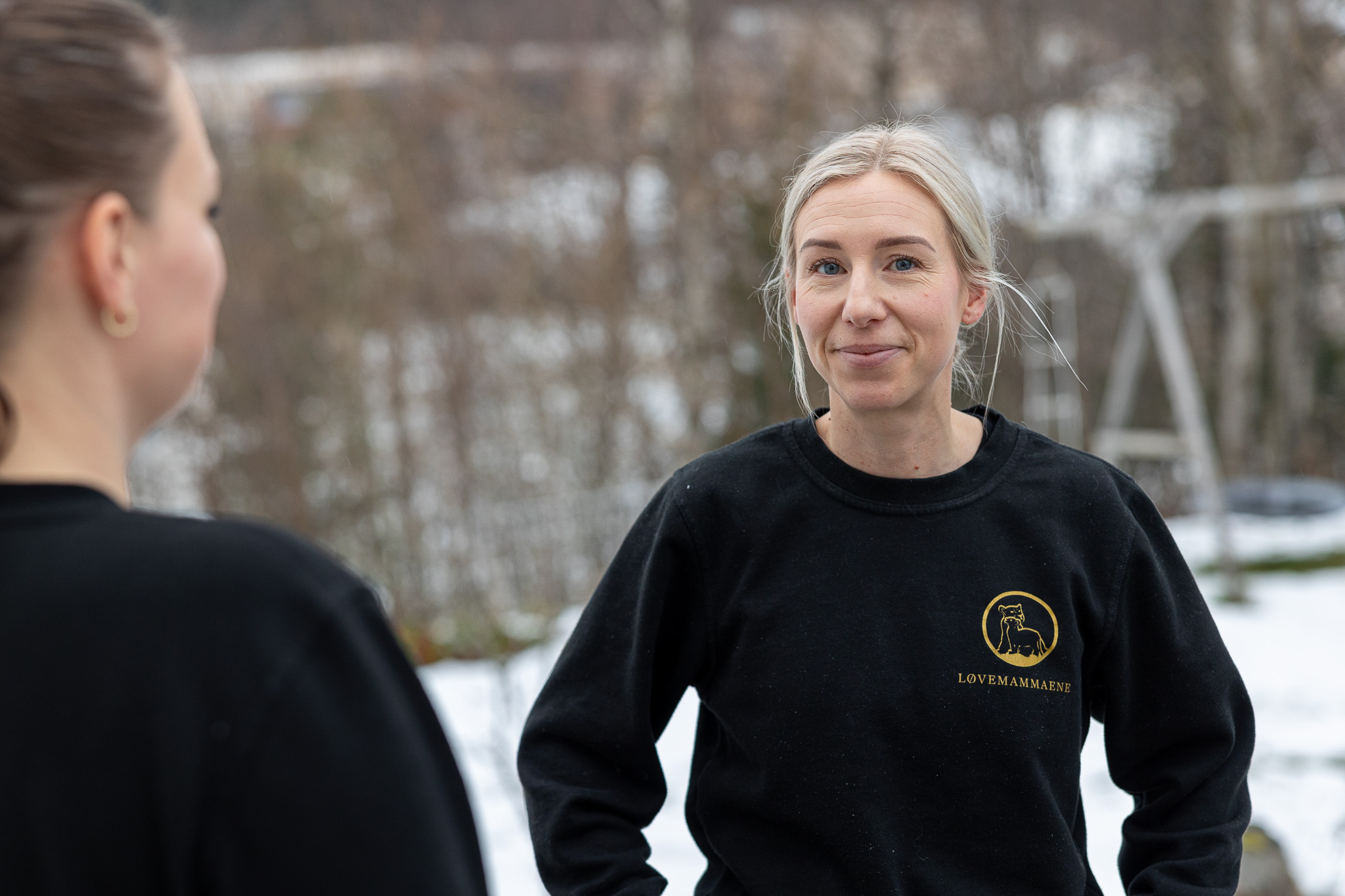 En kvinne ser alvorlig inn i kameraet. Vi ser også ryggen på en annen kvinne. 