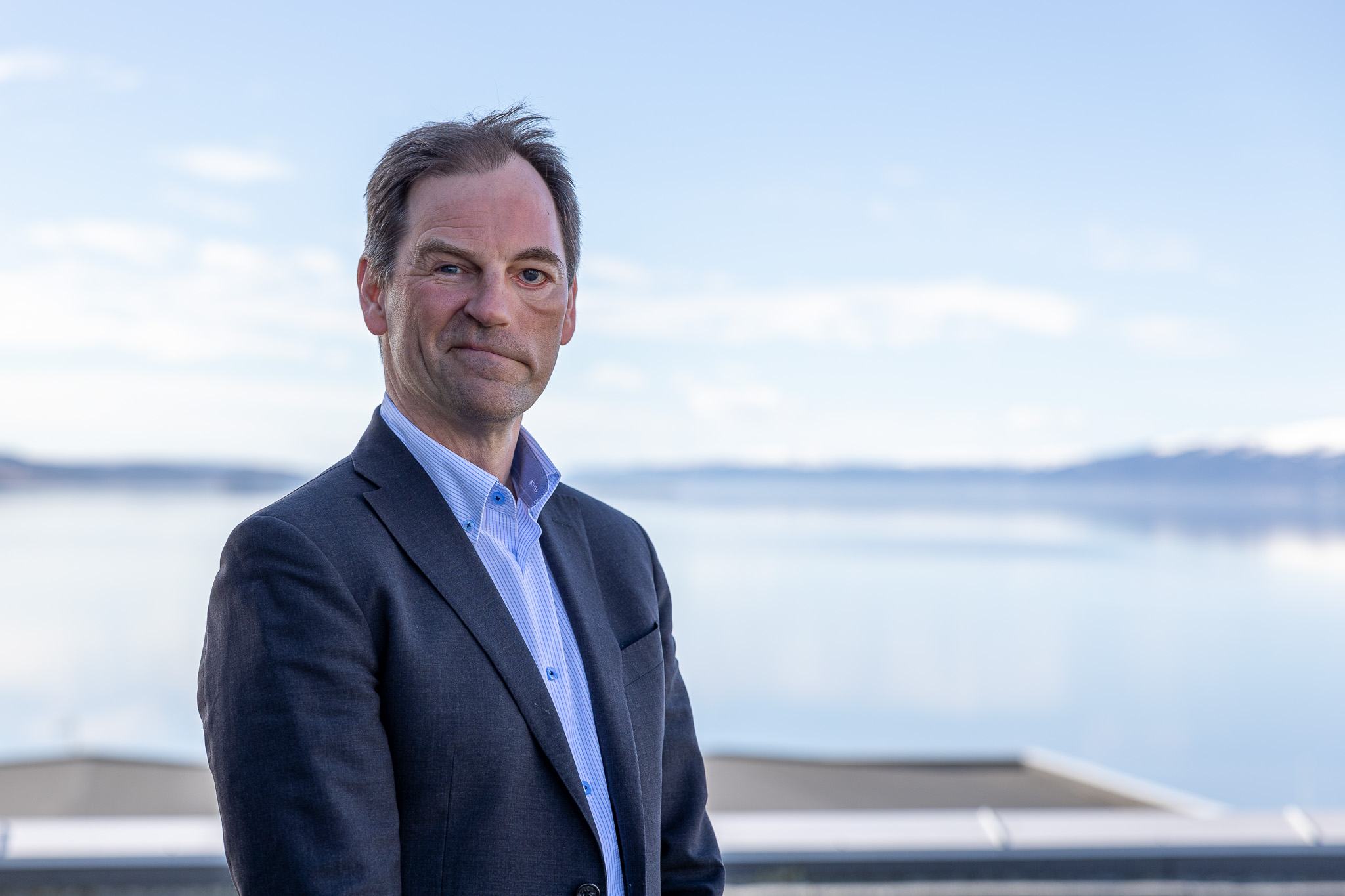 Smilende mann med blått hav og blå himmel bak