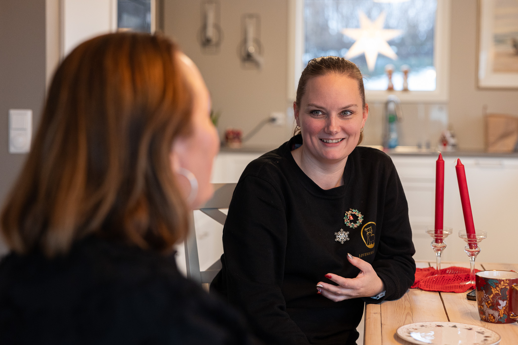 Smilende kvinne i samtale med en person du ser ryggen til. I bakgrunnen henger ei julestjerne. 