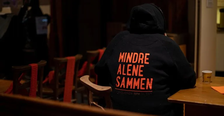 En annerledes julaften Person sitter med ryggen mot kamera der det står "Mindre alene sammen" på hettegenseren