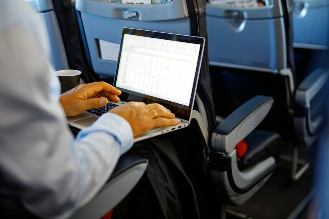 Sikker på reise Bilde som viser ryggen på en mann som sitter i et flysete med en bærbar PC.