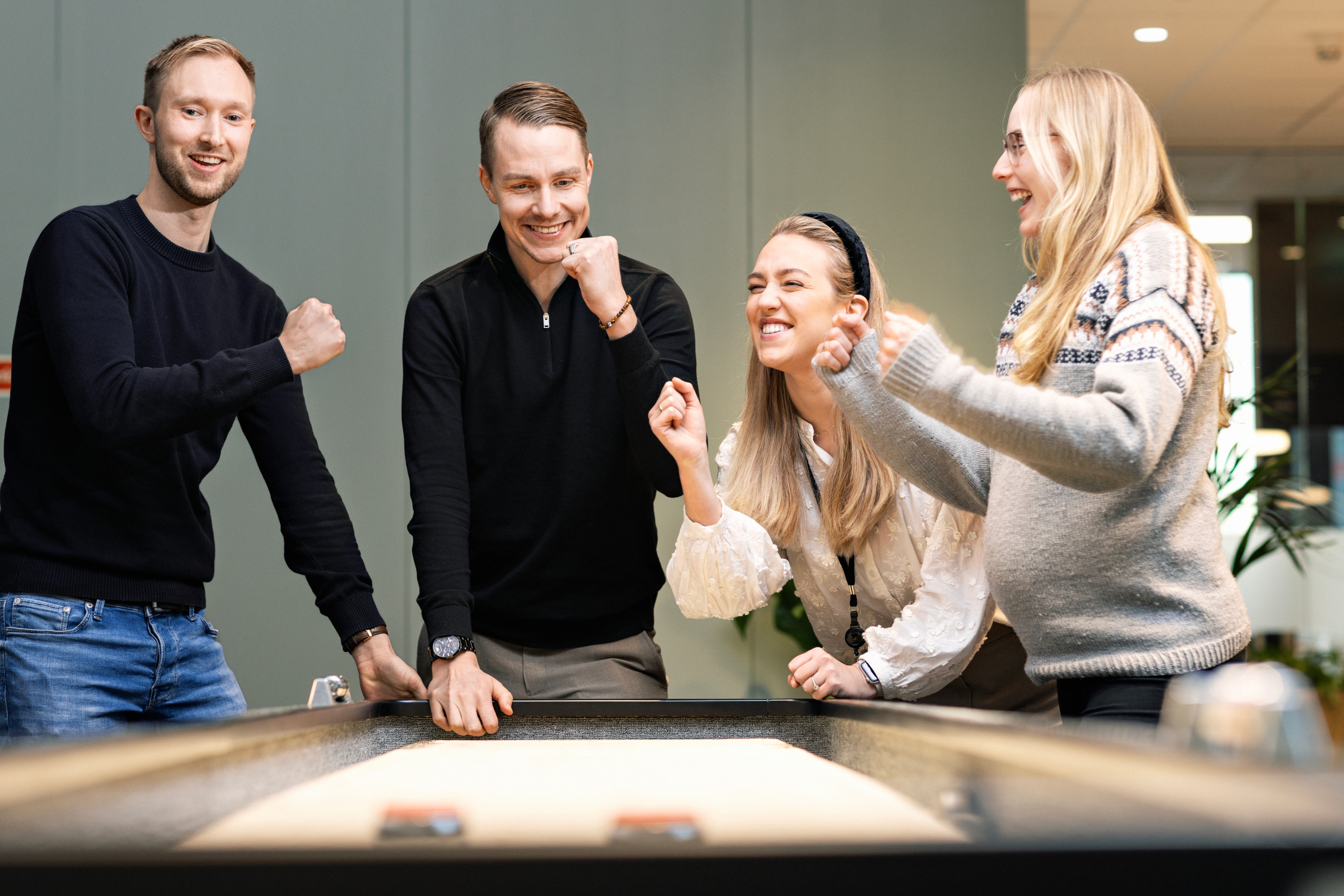 To kvinner og to menn spiller shuffleboard og jubler