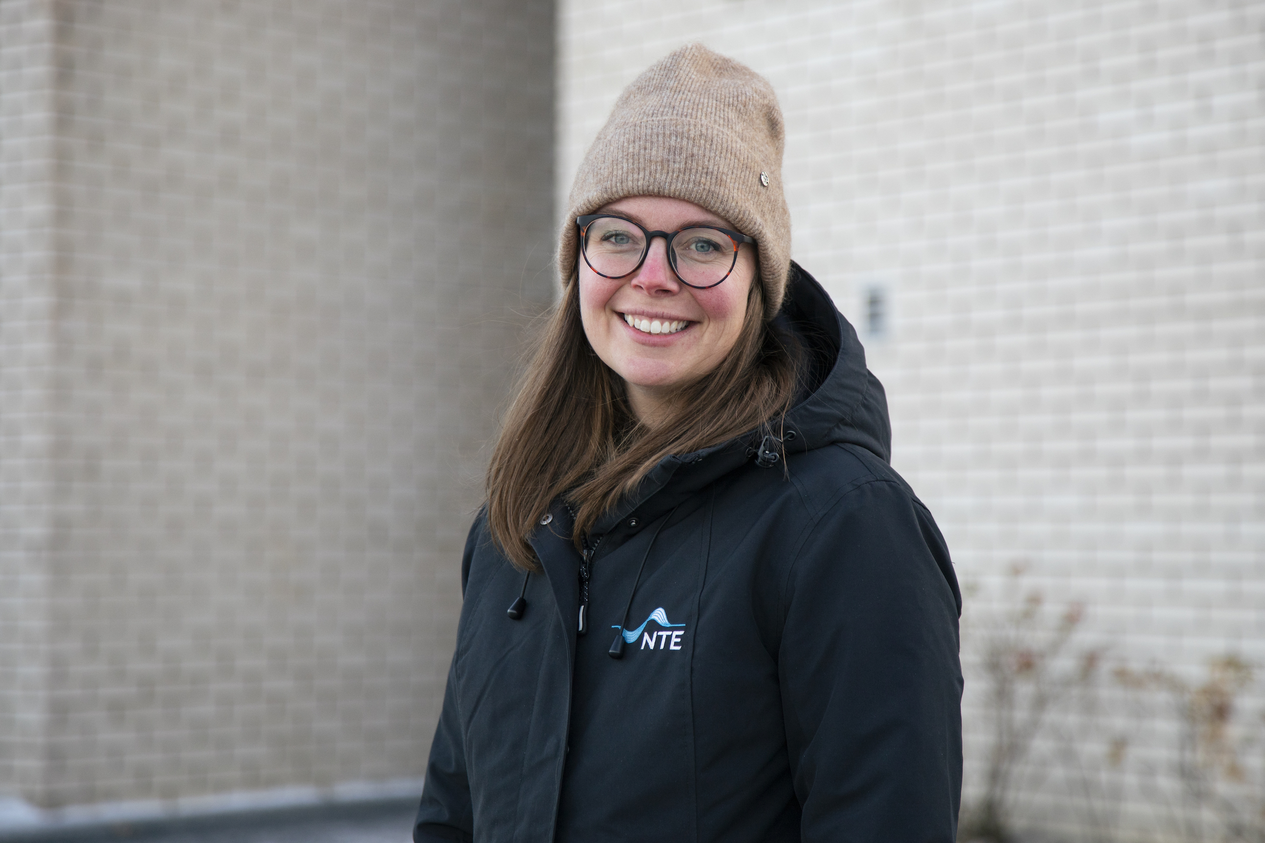Smilende dame med briller, lue og en vinterjakke med NTE-logoen på