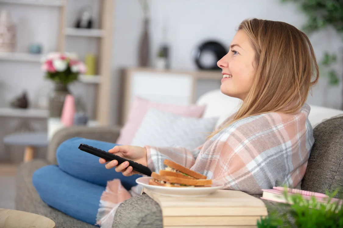 dame ser tv dame ligger i sofaen og ser tv med en brødskive på bordet ved siden av seg