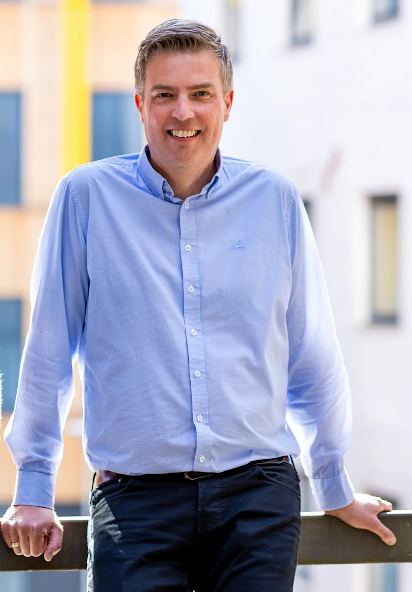 christian jenssen nte Smilende mann i blå skjorte lener seg mot et rekkverk