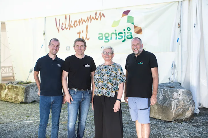 3 menn og en kvinne smiler foran et skilt det står Velkommen til agrisjå på 3 menn og en kvinne smiler foran et skilt det står Velkommen til agrisjå på