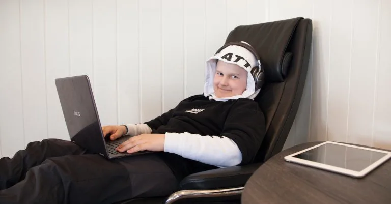 Gutt med pc i fanget Sittende gutt med hodetelefoner og en laptop i fanget