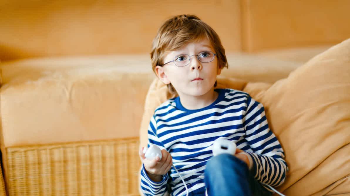 Gutt sitter pÃ¥ sofa og gamer pÃ¥ en TV utenfor bildet