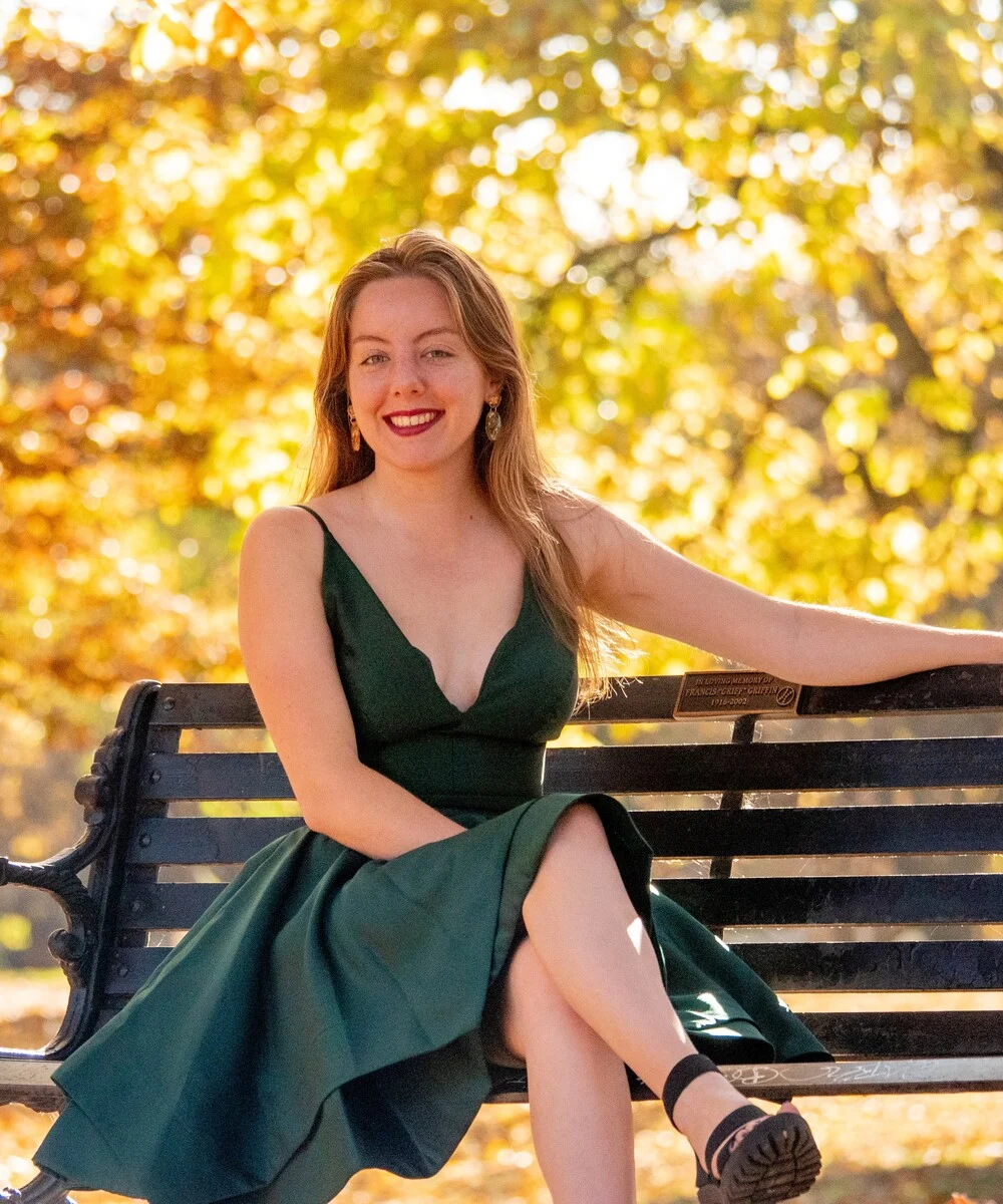 Seated pose in green dress with warm autumn foliage bokeh and golden hour lighting