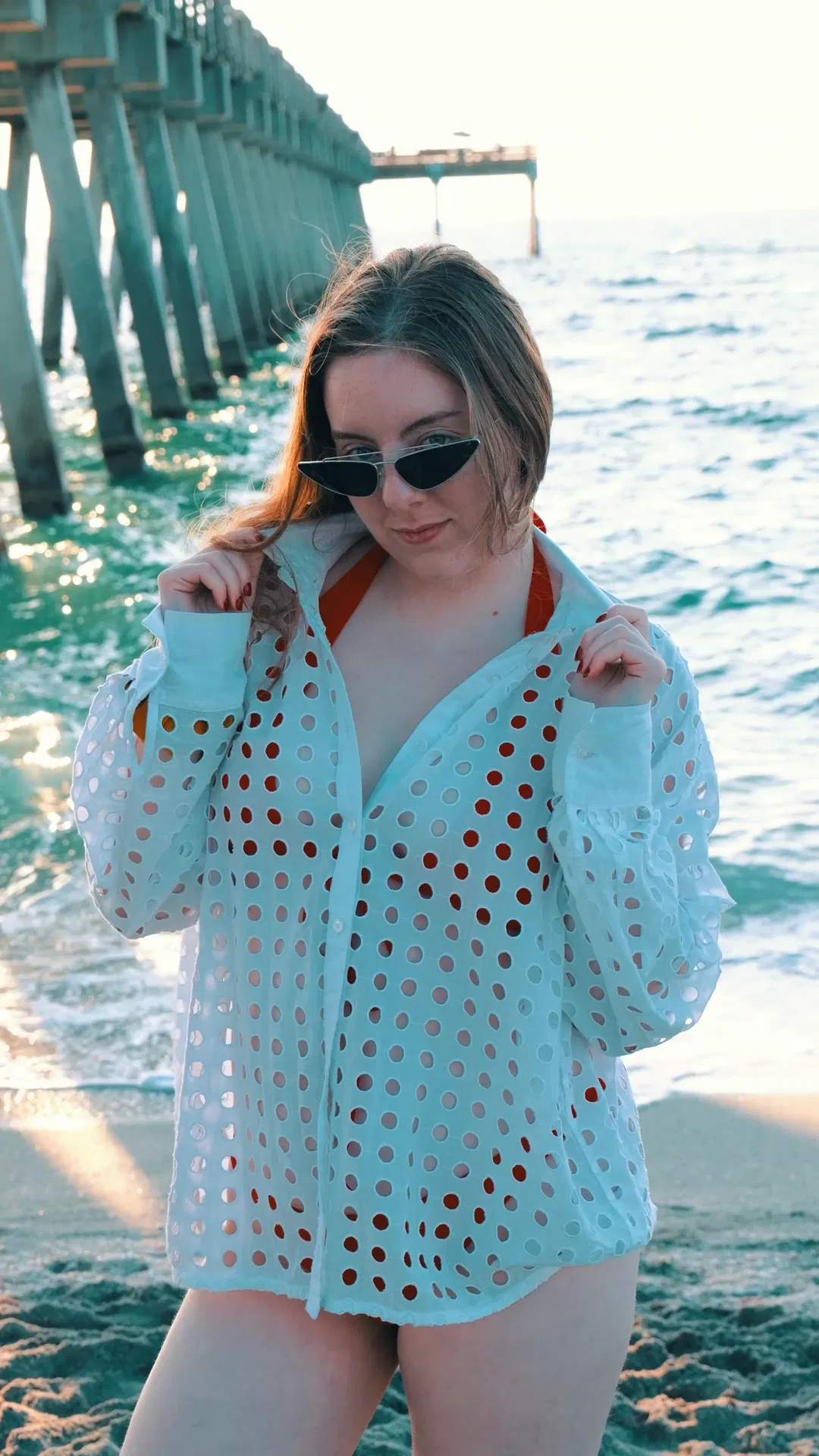 Model in white cutout cover-up and sunglasses at teal pier during golden hour