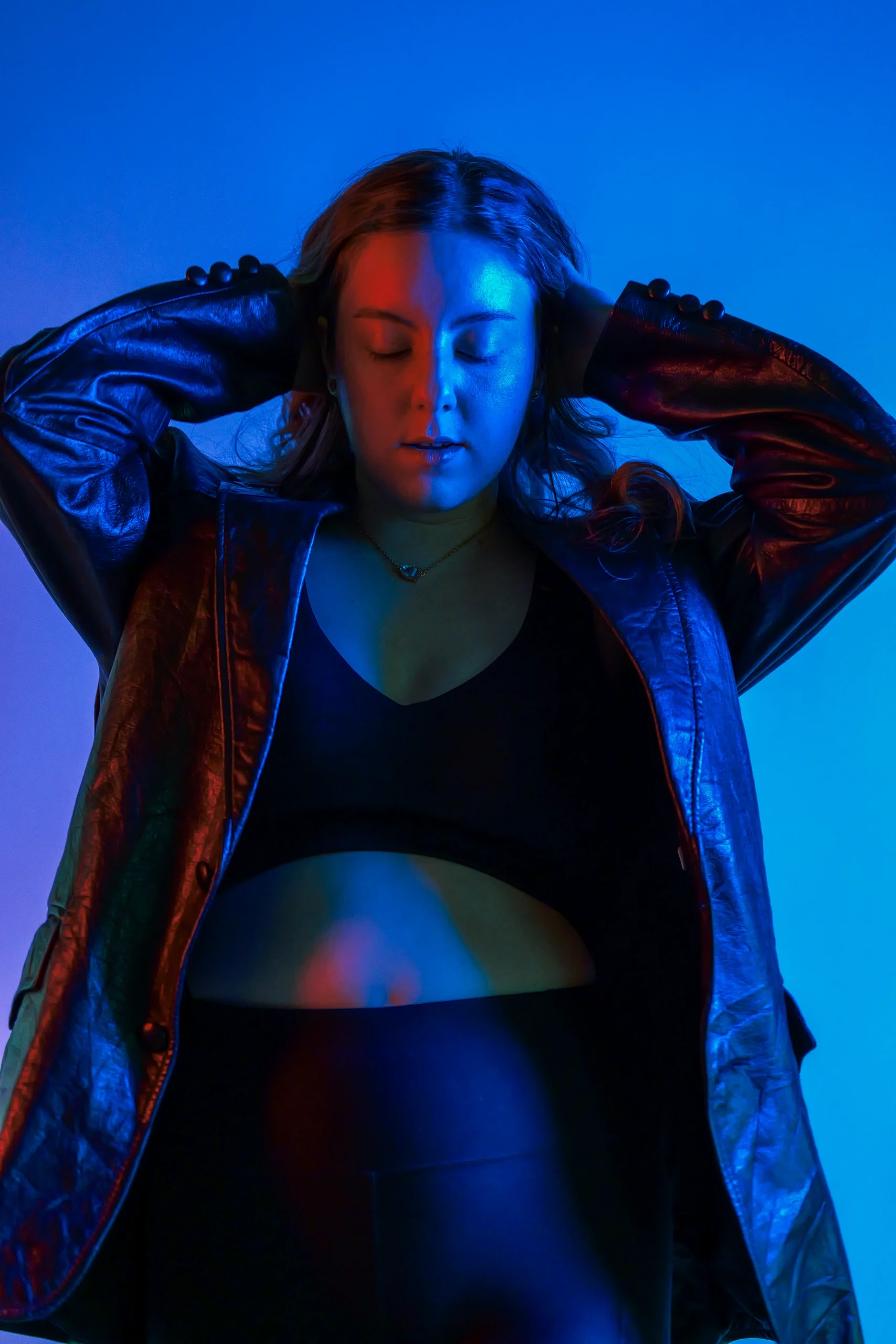 Upward angle with blue and red split lighting, hands to head, leather jacket