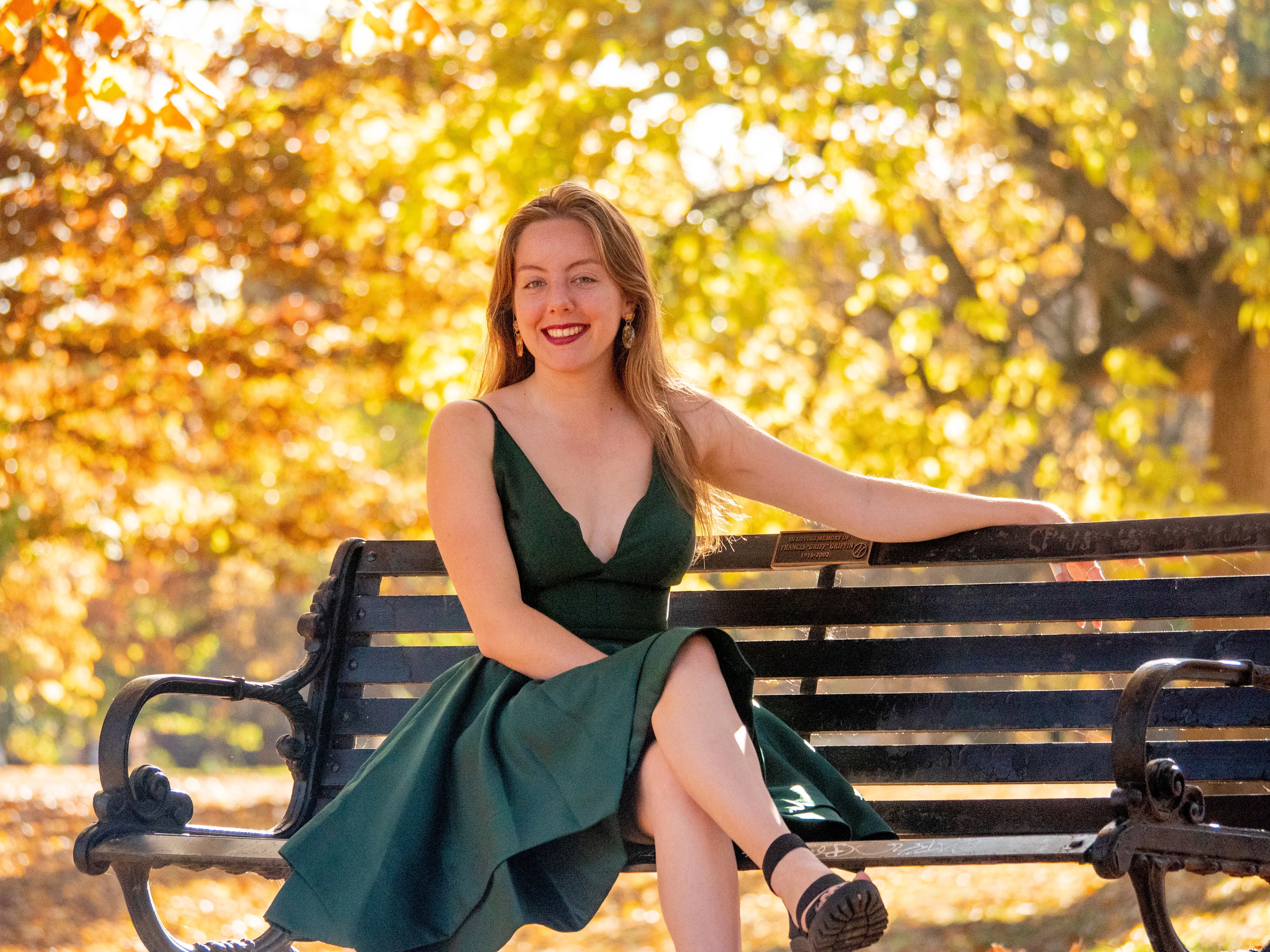Seated pose in emerald dress with golden autumn foliage bokeh and warm lighting