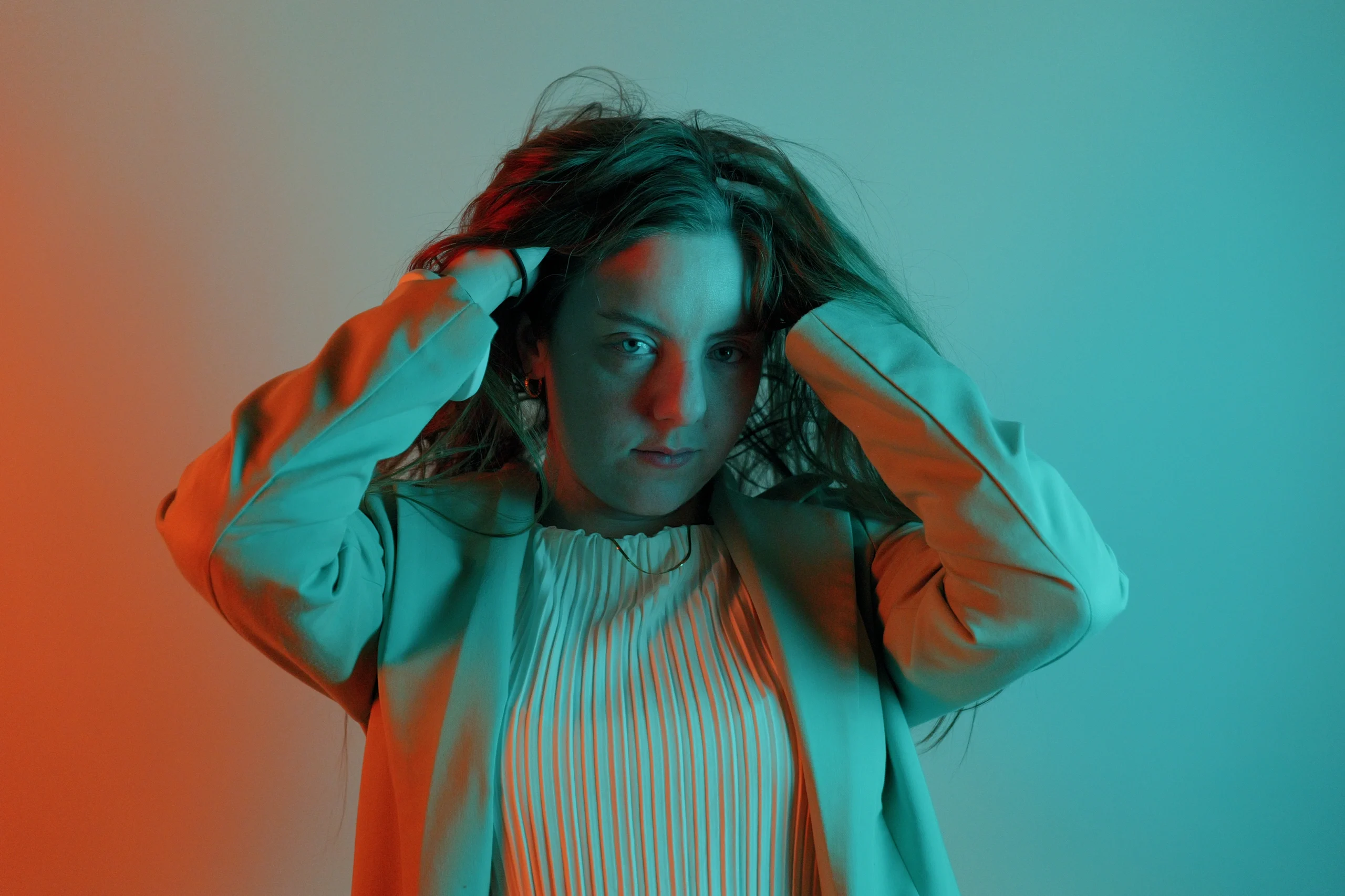 Studio portrait, hands in hair, split cyan-orange gel lighting, white pleated blouse
