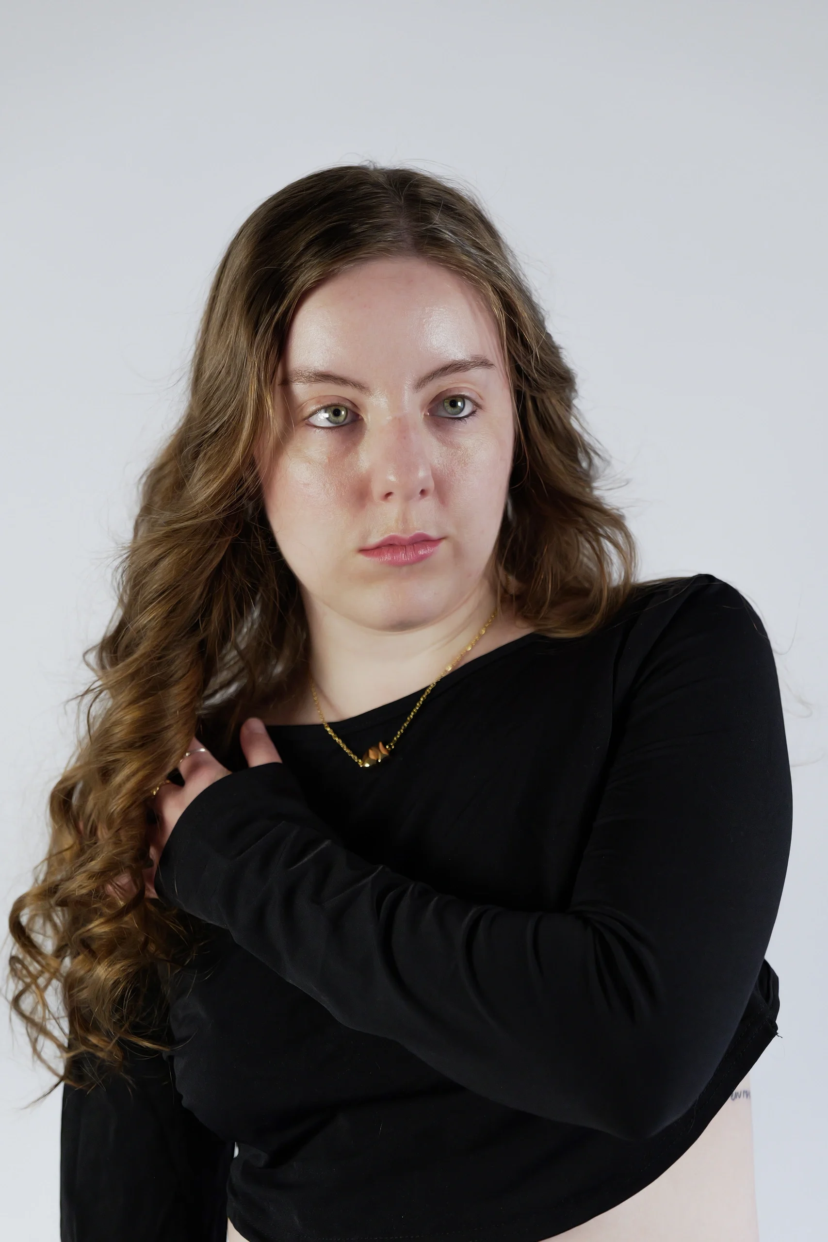 Studio portrait with crossed arms, long wavy hair, black top, and gold necklace