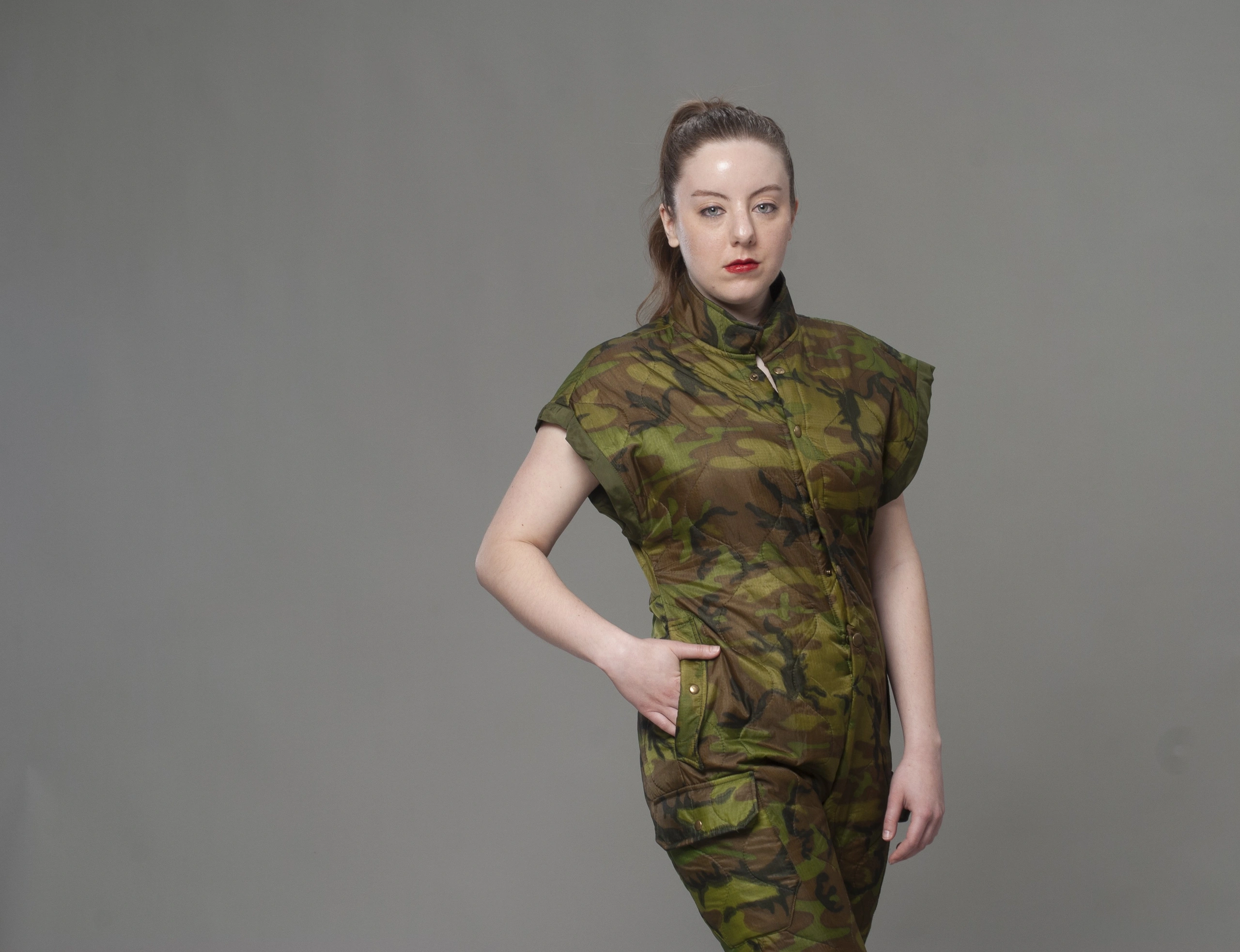 Studio portrait in camouflage uniform with hand on hip against neutral gray backdrop