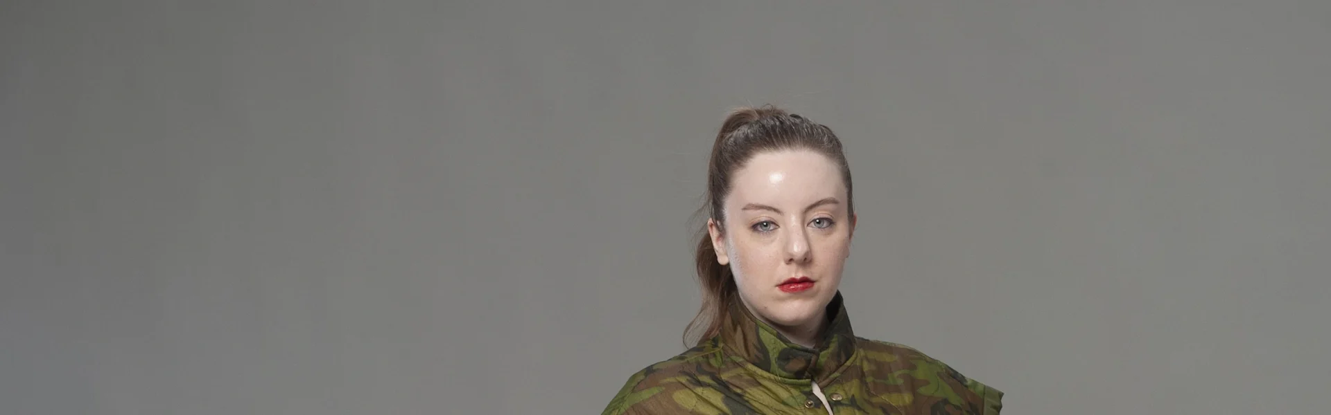 Studio portrait in camouflage uniform with hand on hip against neutral gray backdrop