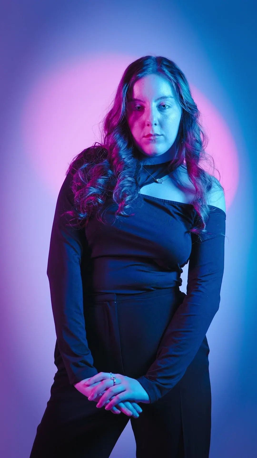 Three-quarter studio portrait with dual-tone lighting and black long-sleeve outfit, hands clasped