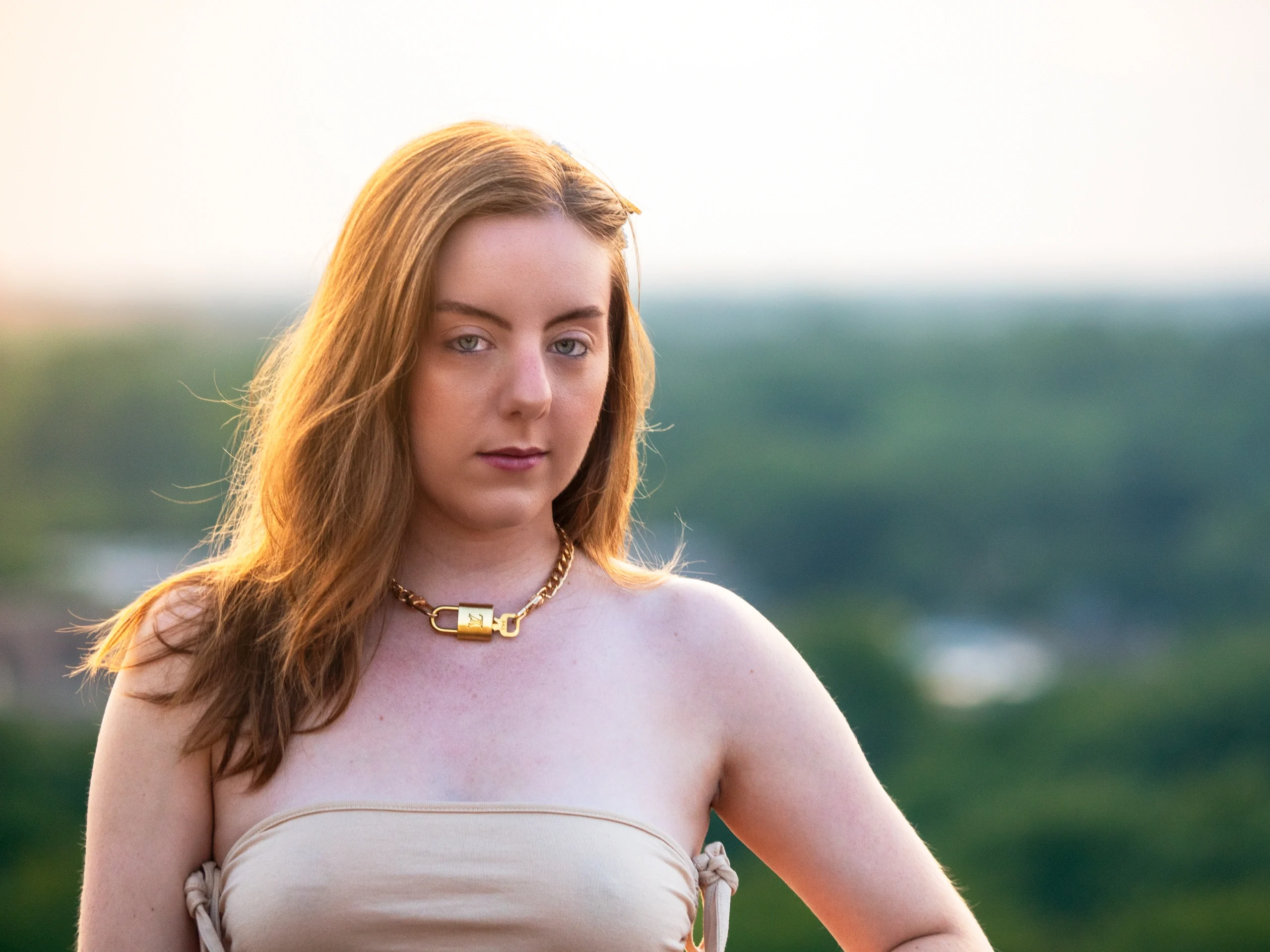 Direct camera gaze with golden rim lighting and statement necklace outdoors at sunset