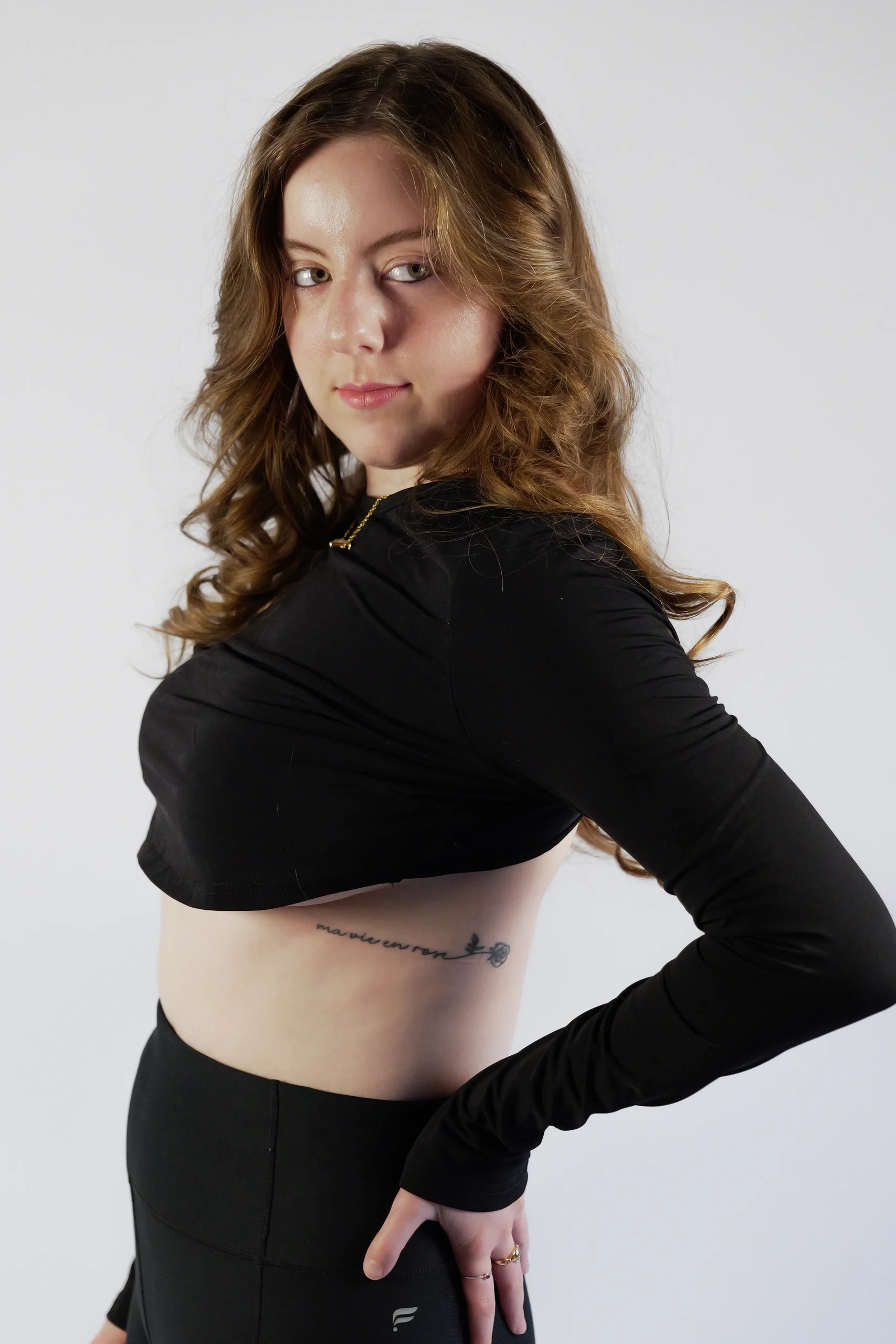 Model looking over shoulder in black long-sleeve crop top and pants against white studio background