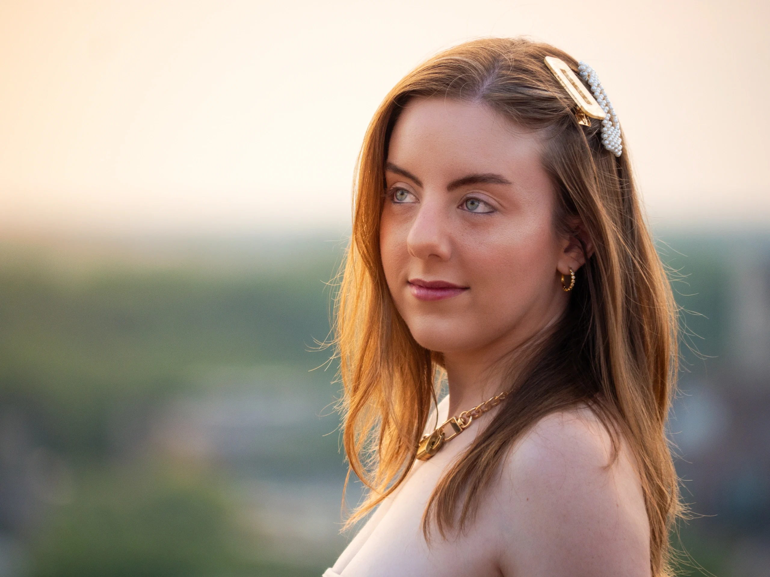 Headshot with pearl hair clip and gold necklace in warm sunset light with cityscape background